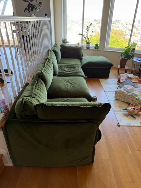 1. Green velvet sectional sofa with plush cushions placed near large windows and indoor plants in a bright room.