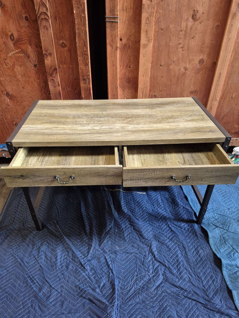 2. Desk with metal legs and wood finish, two open drawers in the center, set on a blue padded surface.