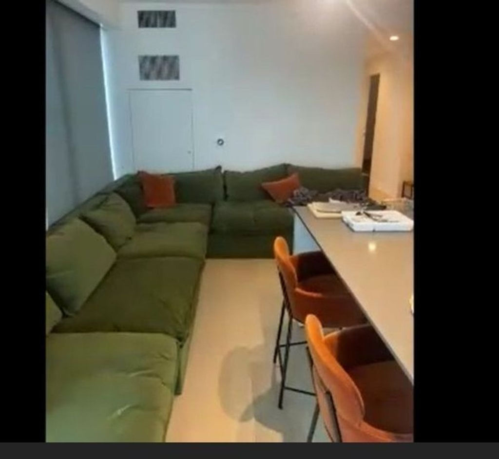 Green sectional sofa in good condition, paired with orange chairs in a modern living and dining open space.