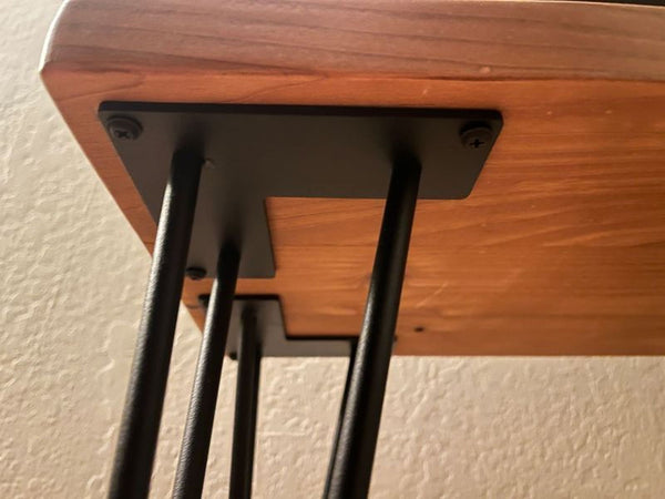1. Close-up of a Reperch stool's black metal hairpin leg attached to a wooden seat with visible screws.