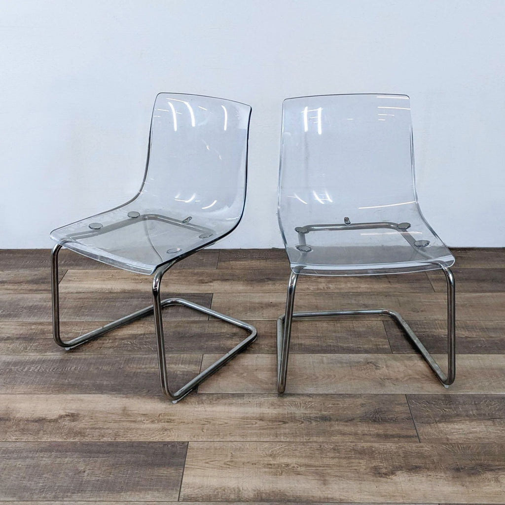 1. Pair of clear acrylic Reperch dining chairs with chrome base, displayed on wood flooring.
