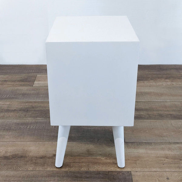 White end table by Reperch with slender legs on a wood floor.