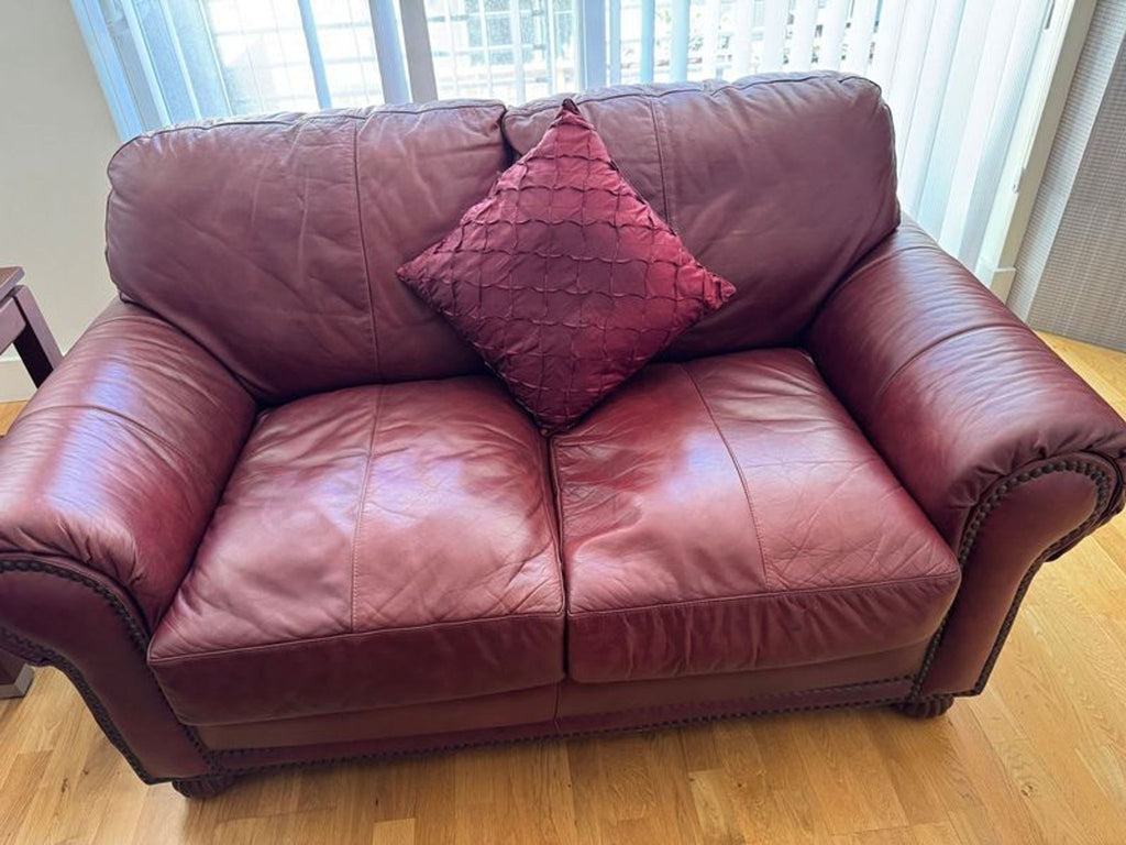 1. Reperch Loveseat with maroon leather upholstery and a matching textured throw pillow, placed in a sunlit room.