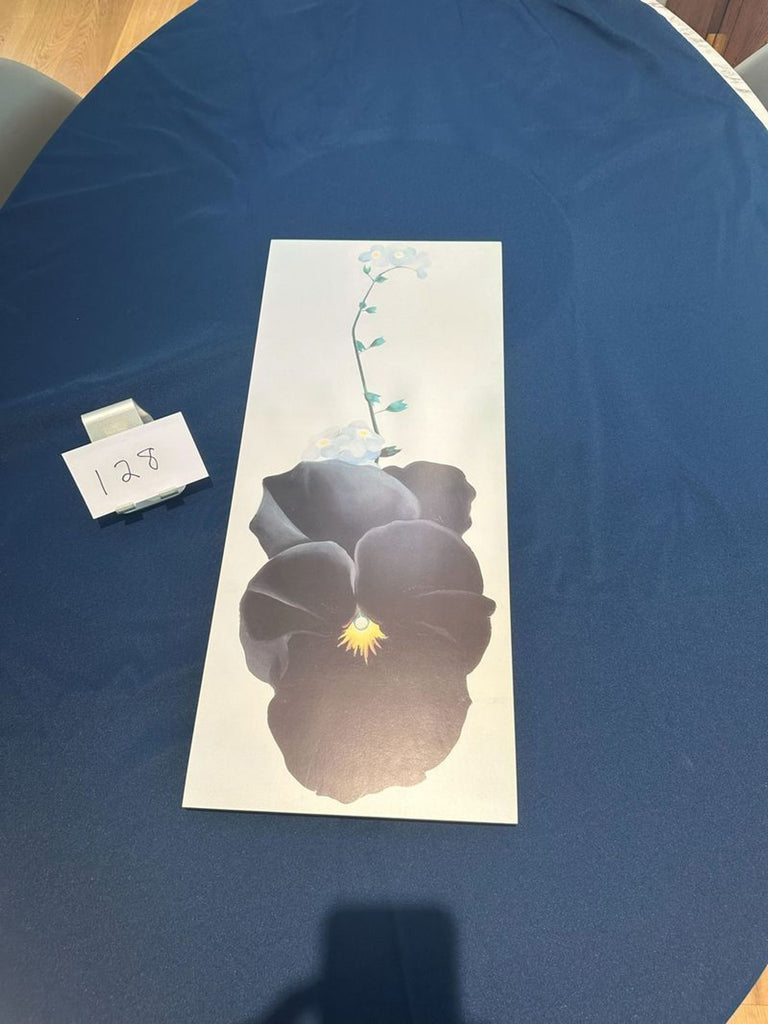 1. Vertical floral painting with a large dark flower and delicate stem, placed on a blue tablecloth near a "128" card.