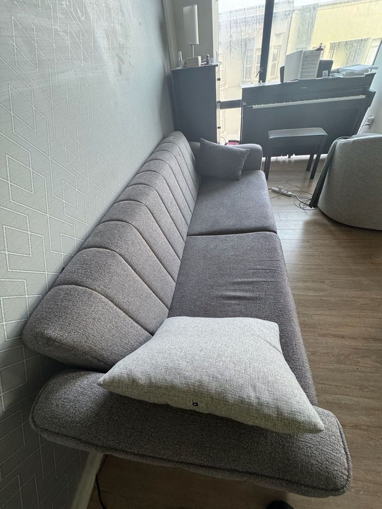 1. Modern gray 3-seat sofa with two cushions in a living room, placed against a patterned wall and near a window.