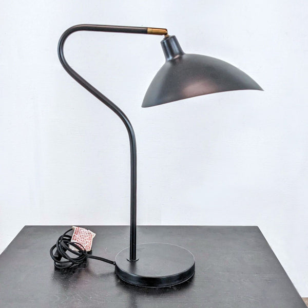 Modern black desk lamp with curved neck and round base, showing slight age wear.