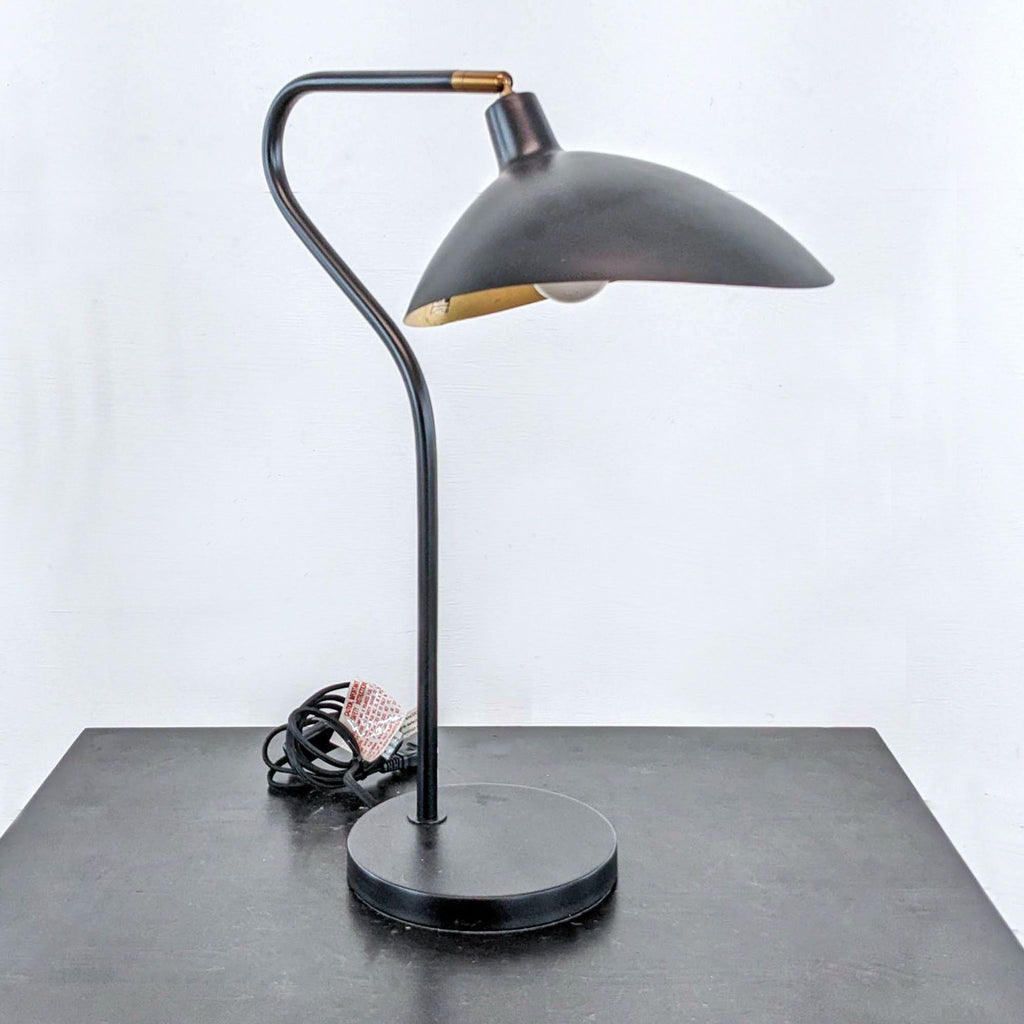 Elegant black desk lamp with a sleek design and brass accent, resting on a black base.
