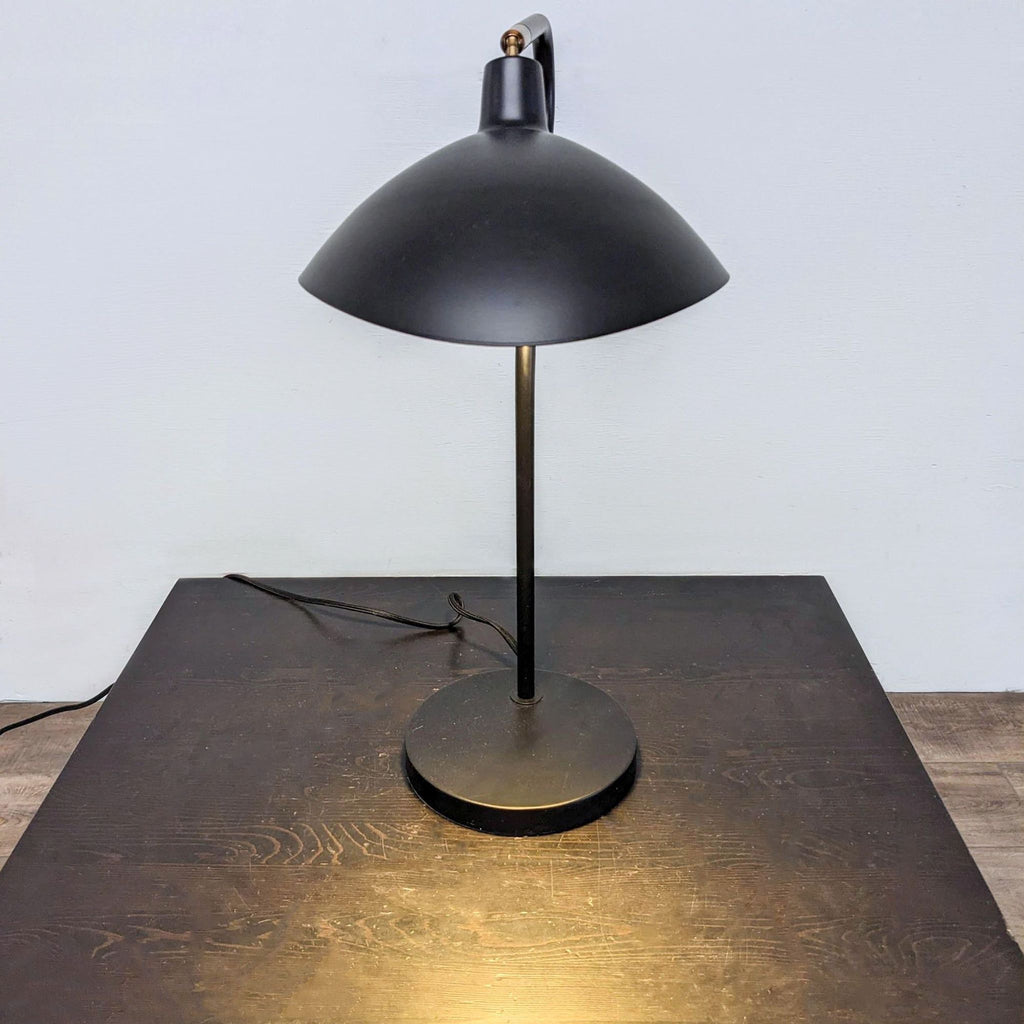 Stylish black lamp with a wide shade, emitting a focused light onto a dark table surface.