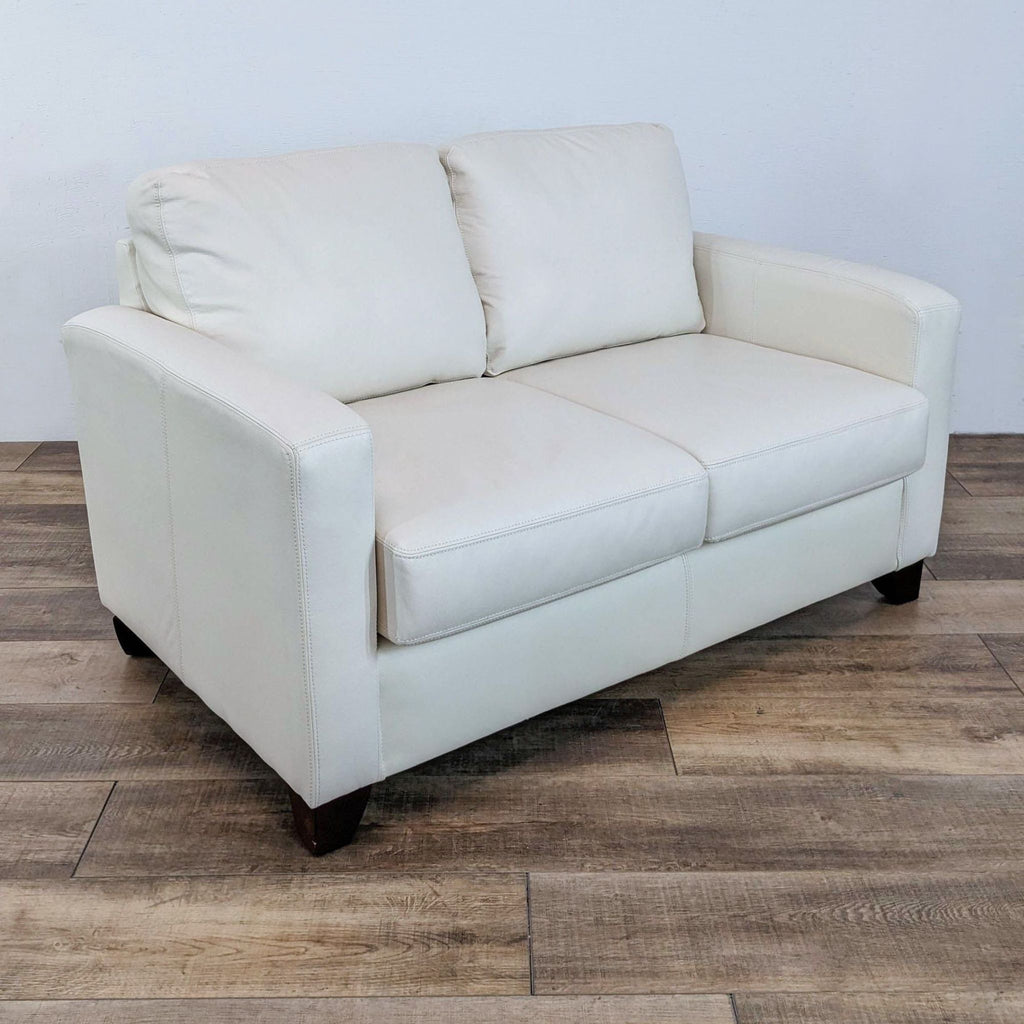 2. Angled side view of a modern white loveseat featuring track arms and dark wood feet from Sofa By Fancy.