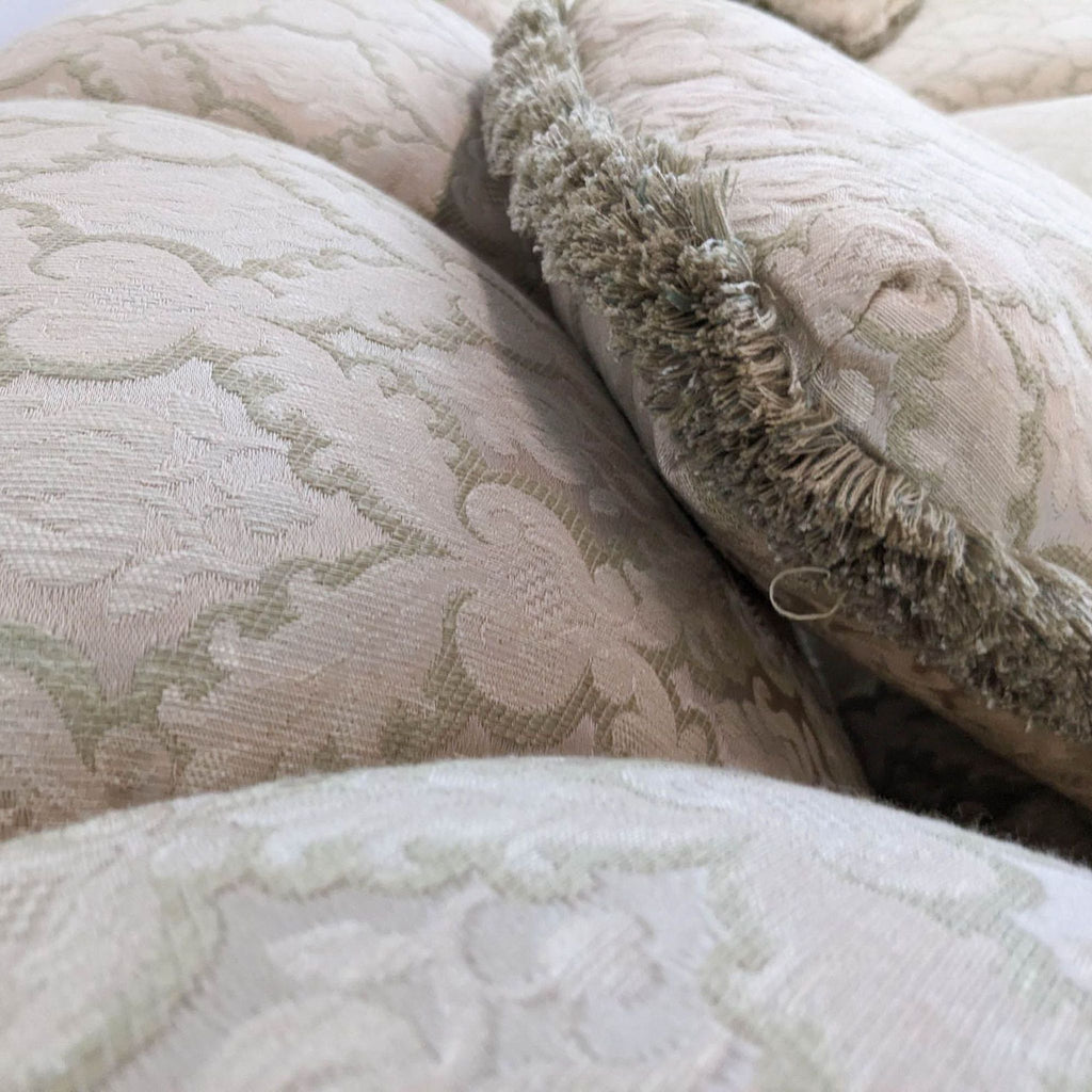 Close-up of floral damask fabric with fringed edges on a vintage sofa cushion.