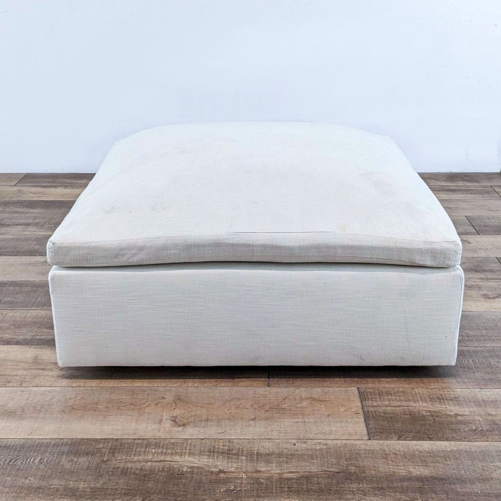 Square ottoman with deep cushion, in performance linen on wooden floor.
