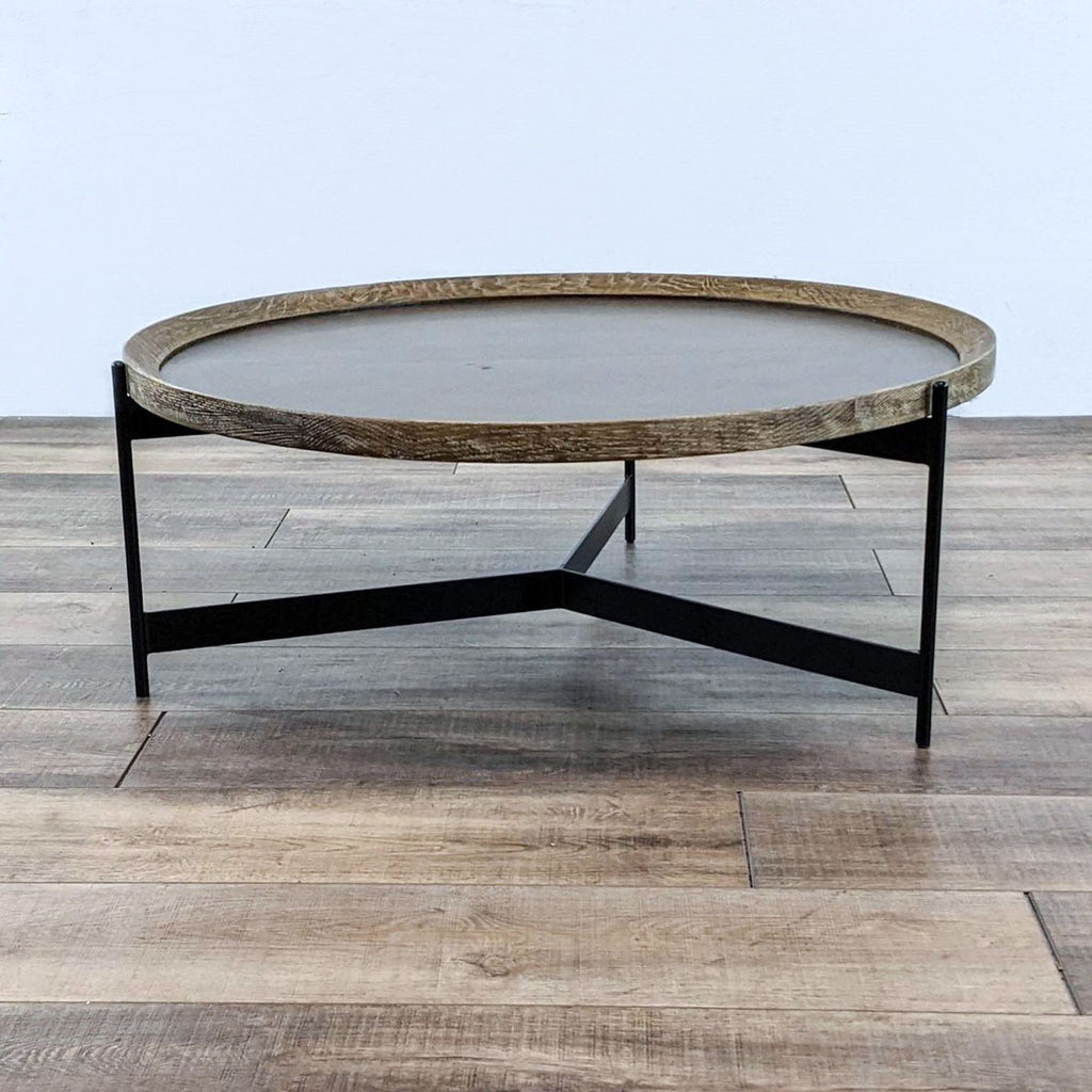 Round coffee table with a brass-clad top and oak-finished trim on black iron legs.