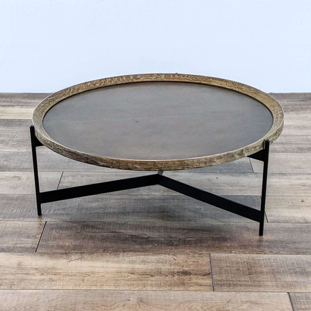 Side view of round coffee table with oak trim and black powder-coated iron base.
