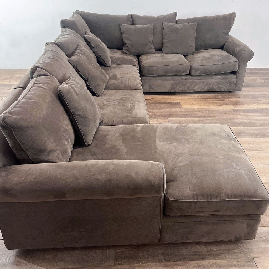 Gray corner sectional with chaise, featuring thick cushions and high back pillows on wooden floor.