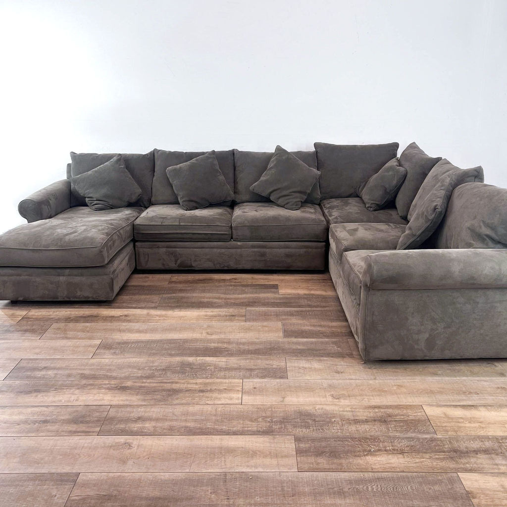 Modular sectional with chaise in gray, rounded arms, high back pillows on wooden floor.
