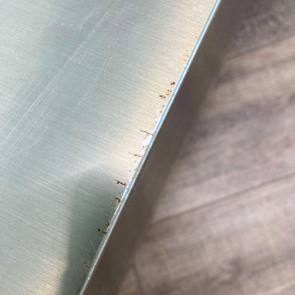 2. Close-up of a Mobital coffee table corner showing brushed stainless steel surface with visible rust and wear.
