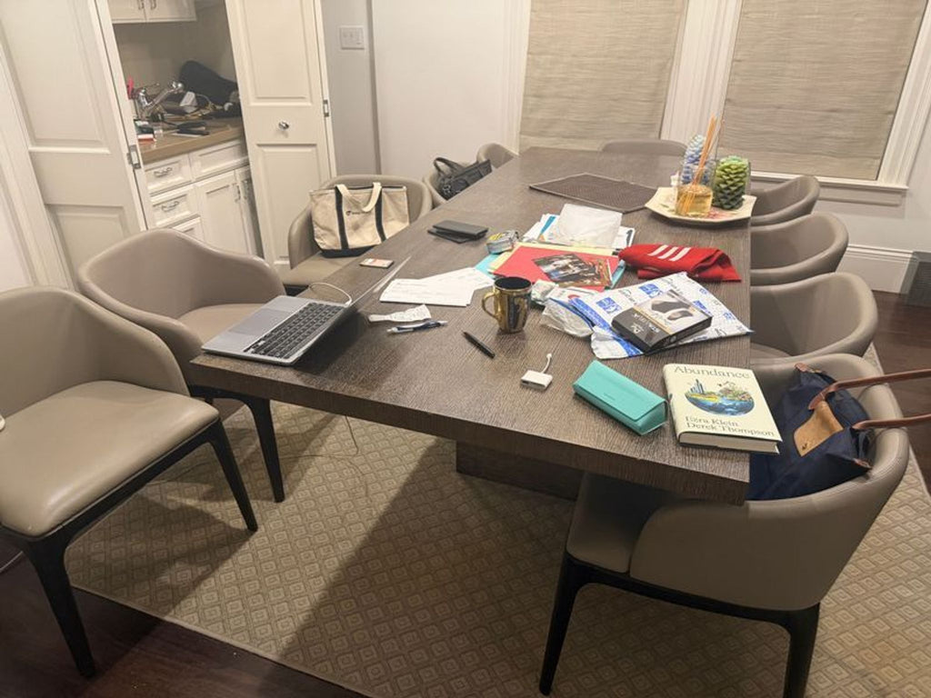 1. Modern dining set with six taupe chairs around a rectangular wood table cluttered with books, laptop, and papers.