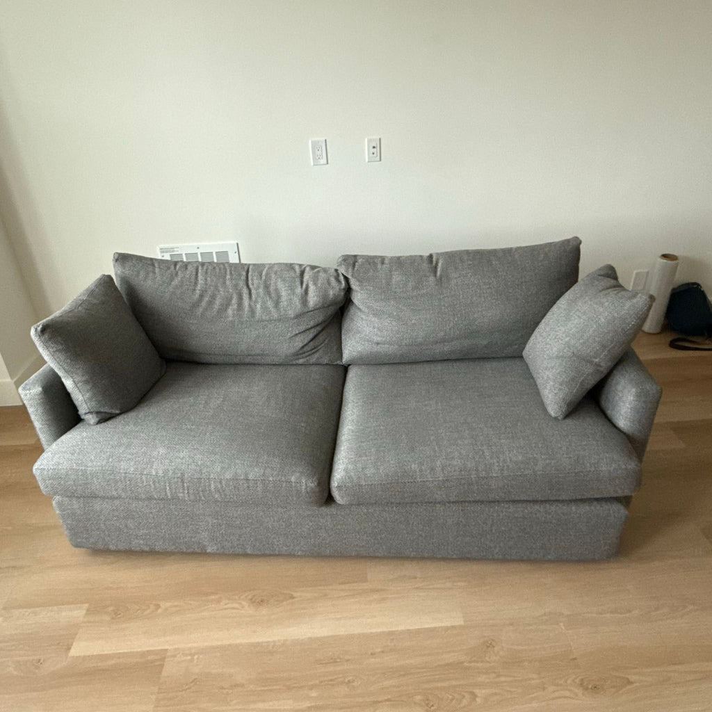 2. Modern gray Crate and Barrel 3-seat sofa with two seat cushions and two pillows on a light wood floor.