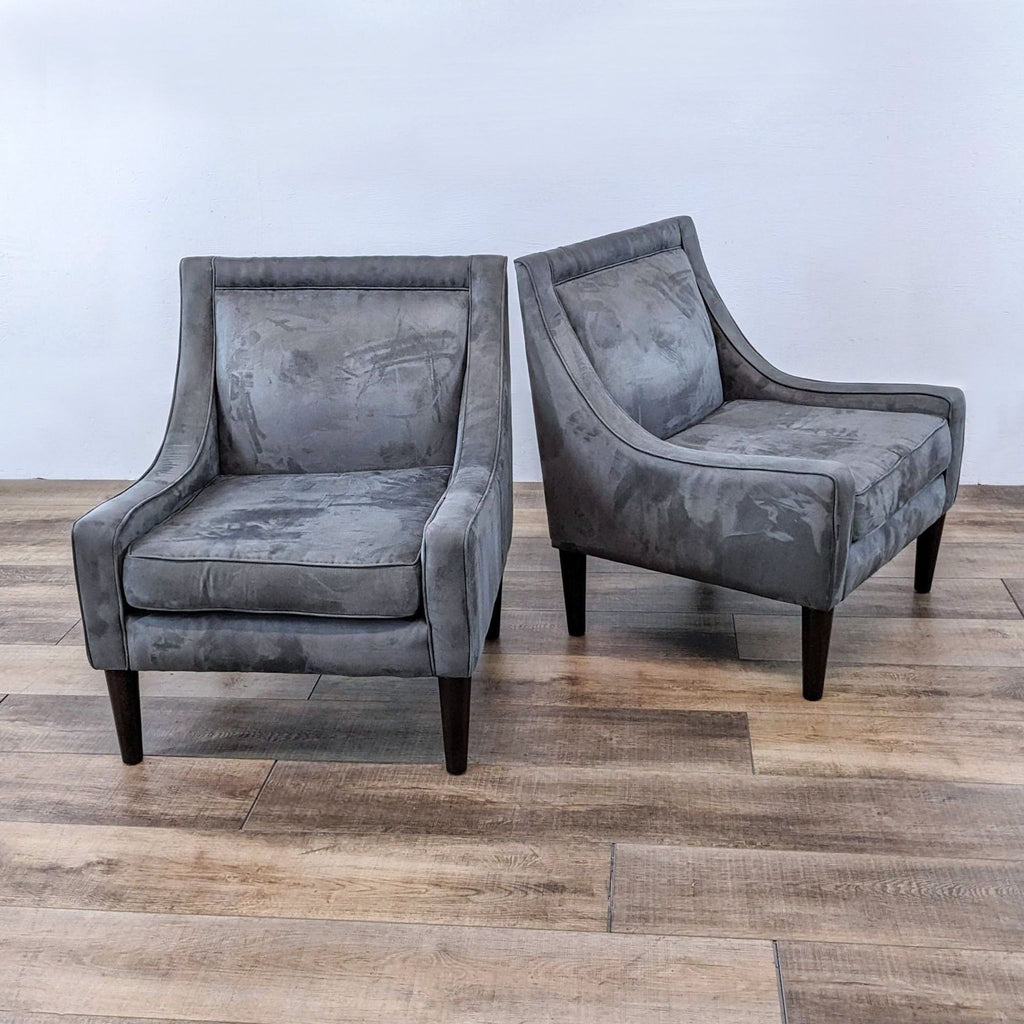 Pair of gray armchairs with sloped arms and wood legs on hardwood floor.
