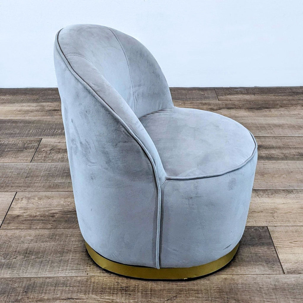 Side view of gray velvet chair with gold base on wood floor.