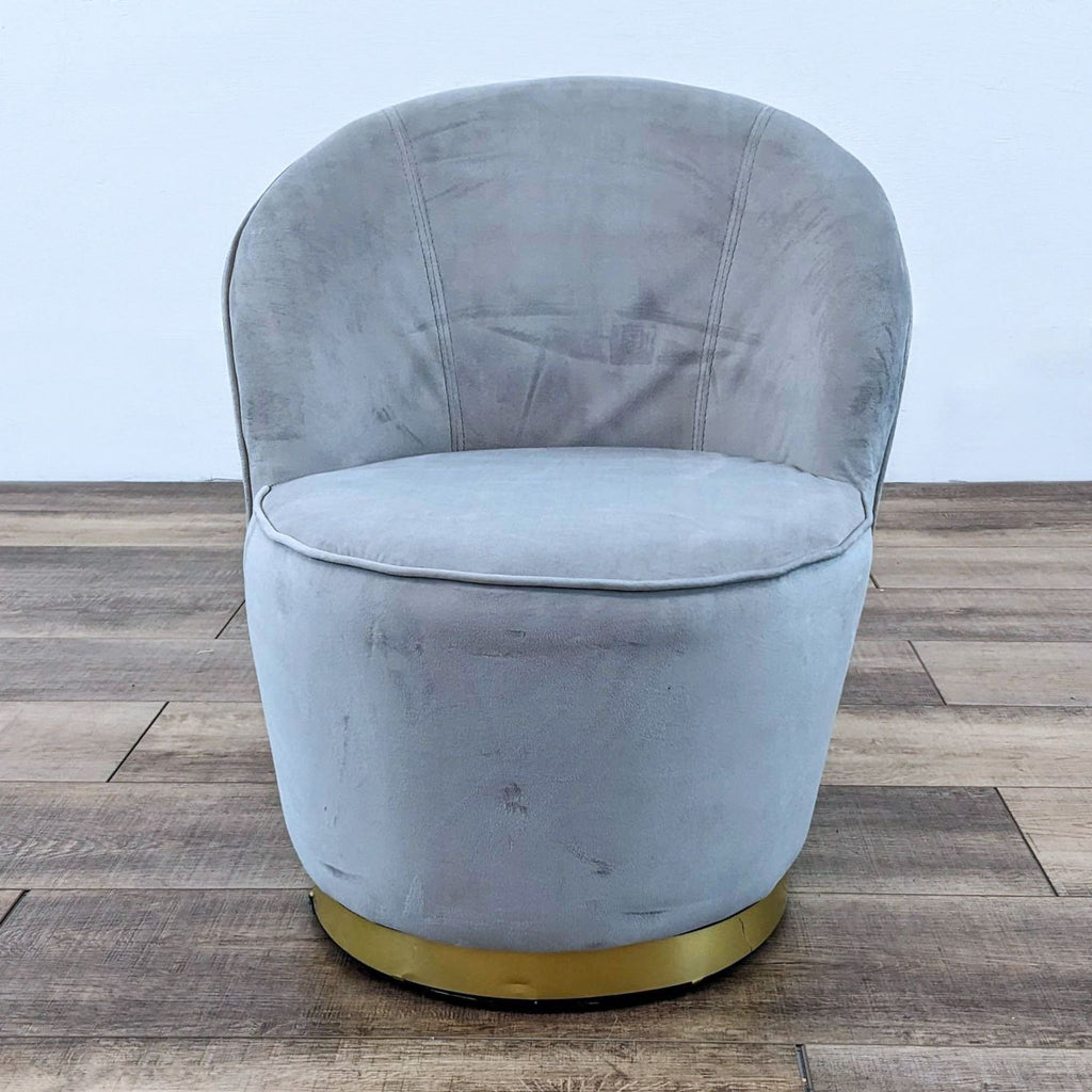 Gray velvet barrel chair with gold base on wooden floor.