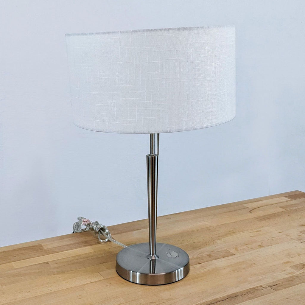 Elegant lamp with a white drum shade and steel pole base on a wooden surface.
