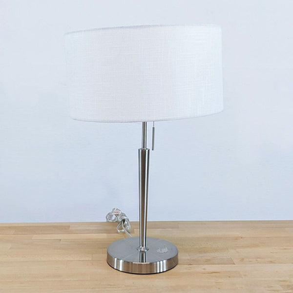 Sleek lamp with a white textured drum shade on a tapered steel pole and pull-chain. 