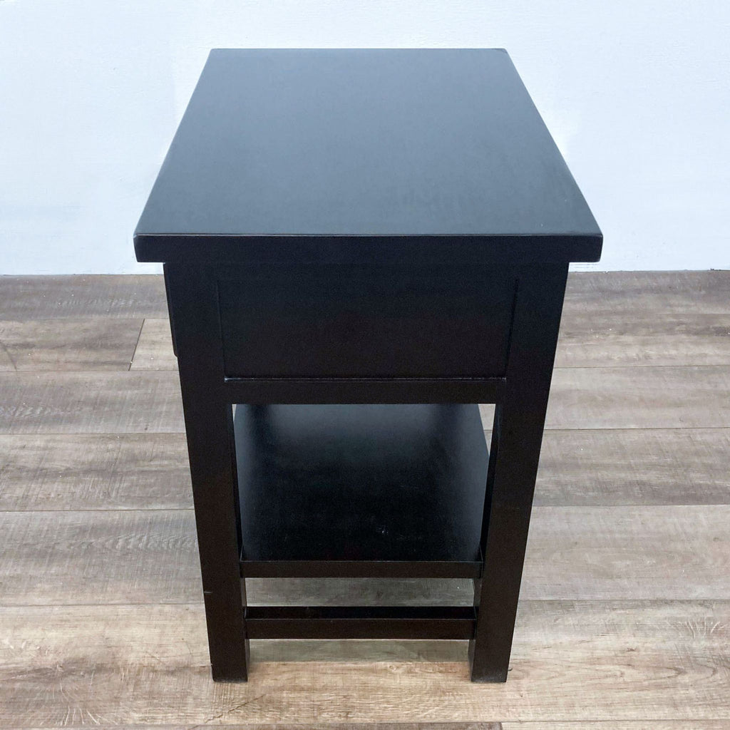 Side view of a dark end table with a lower shelf, on a wooden floor.