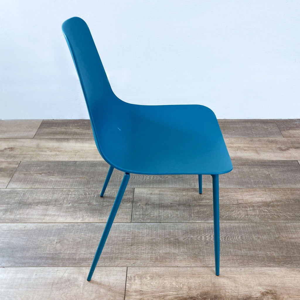 Teal chair with molded plastic seat and metal legs, viewed on a wooden floor.