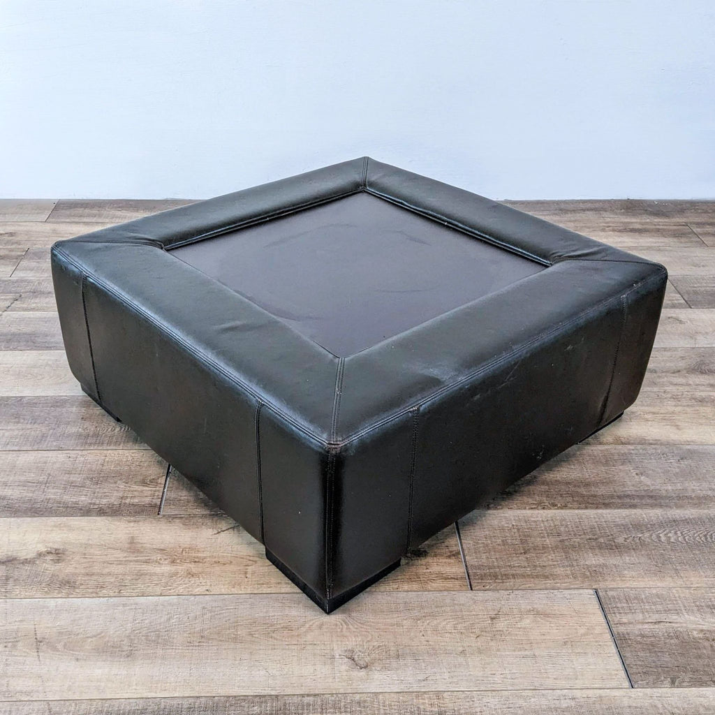 Reperch coffee table in black leather, square design, shown on wooden floor.