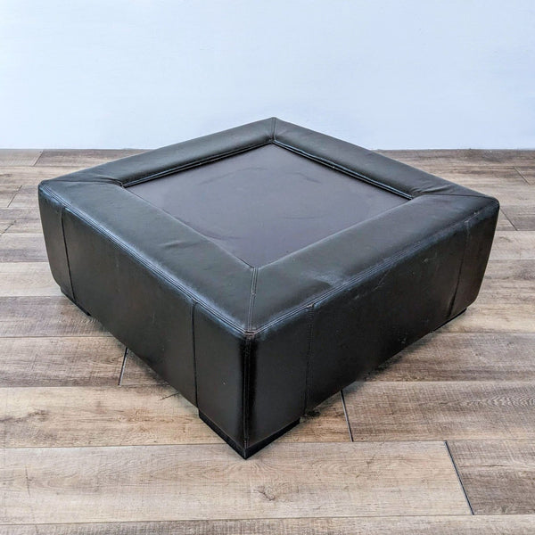 Reperch coffee table in black leather, square design, shown on wooden floor.