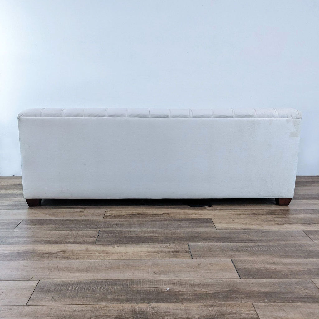 Back view of a tufted off-white sofa with wooden legs, showcasing simple elegance.