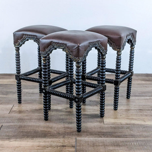 Set of three bar stools with leather seats, wood spindle legs, and nail head detailing.