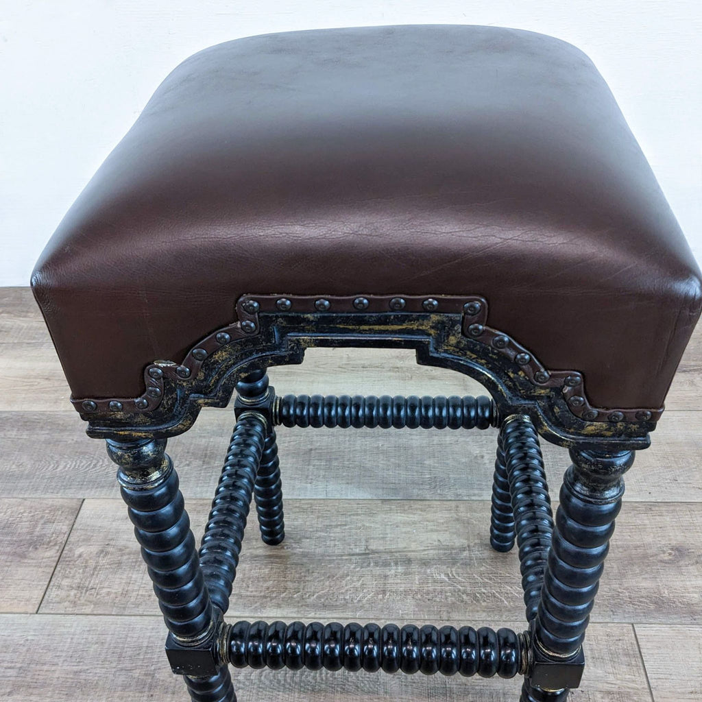 Close-up of a bar stool seat with leather padding, spindle legs, and decorative nail head trim.