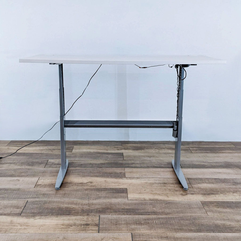 Adjustable height desk with cords visible on a wood floor.