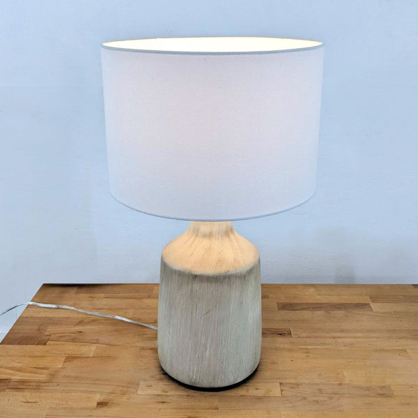 Light gray concrete lamp with a drum shade on a wooden table.