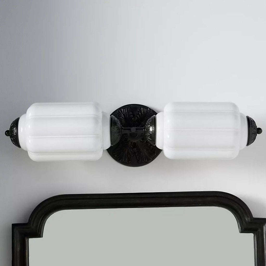 3. Double sconce wall light with white frosted glass shades and ornate black base, mounted above a mirror.