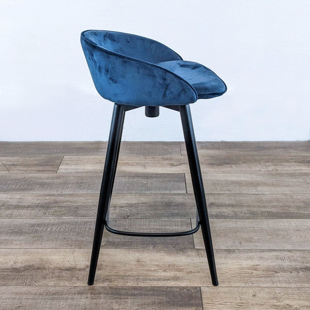 a blue velvet bar stool with a black metal frame and a black metal base.