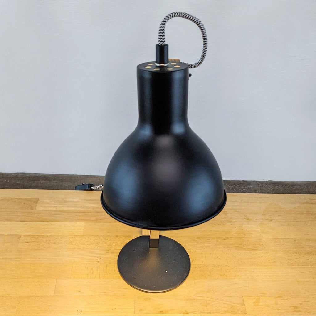 Black metal desk lamp with round base on a wooden surface.