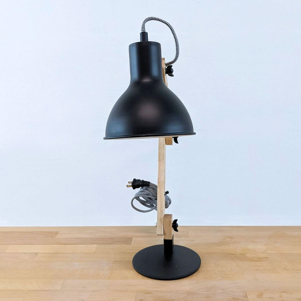 Adjustable desk lamp with black shade and wooden stand on a table.