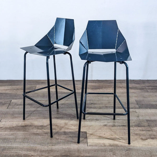 Two modern barstools with geometric steel seats and black legs.