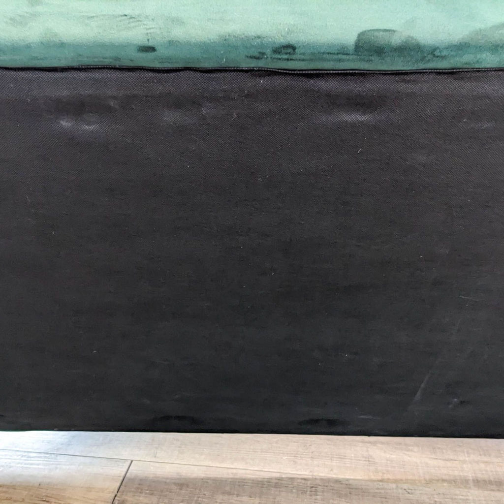 Close-up of the base of a green Reperch sofa on wooden flooring.