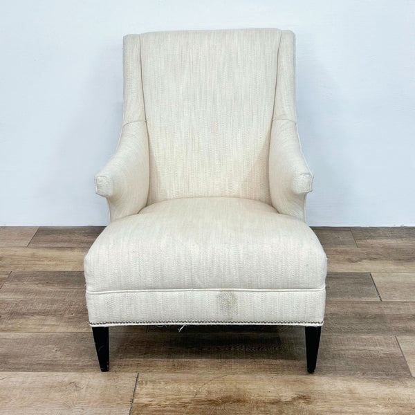 Front view of a cream wingback chair with nailhead trim and dark legs.