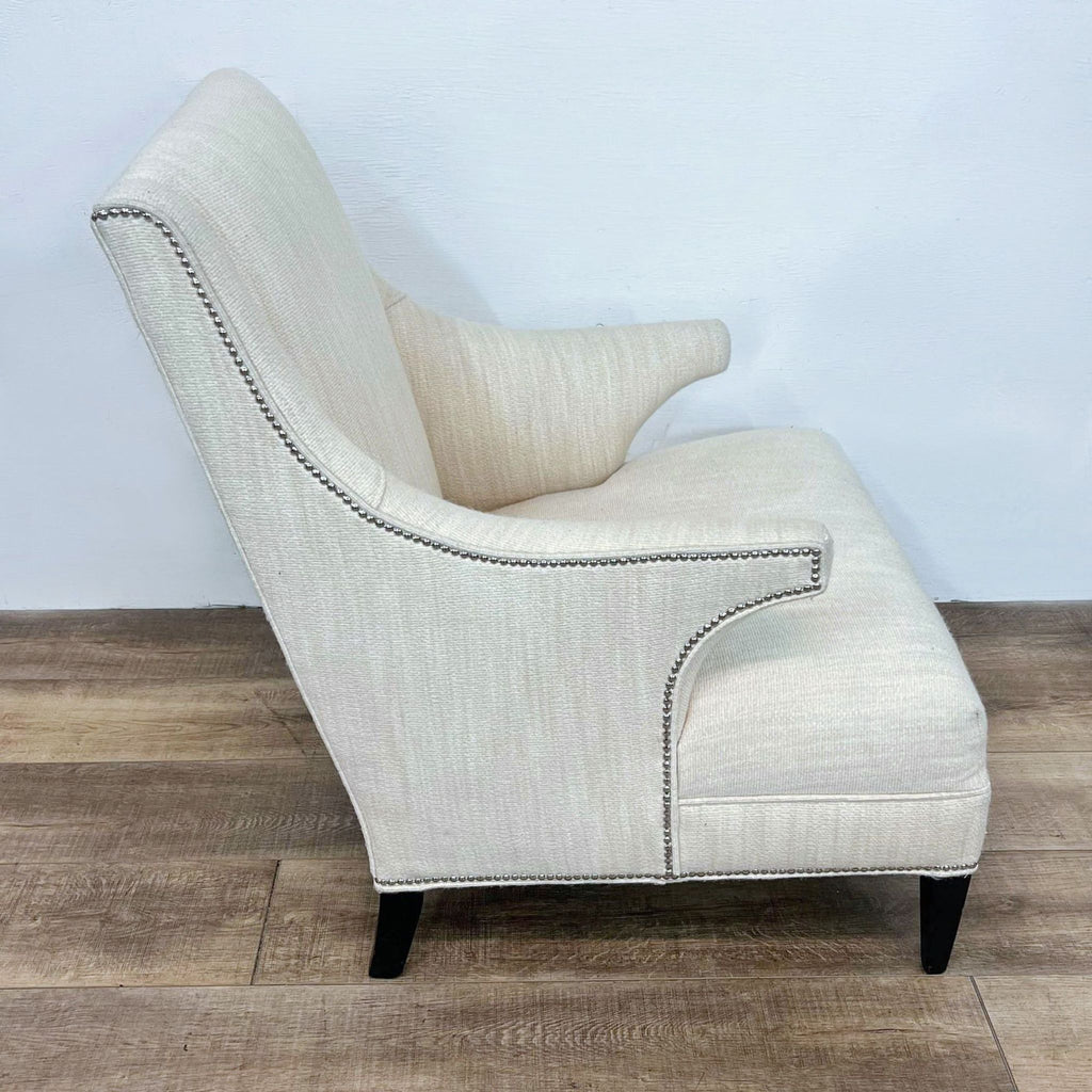 Side view of a cream wingback chair, showcasing nailhead trim and angled armrests.