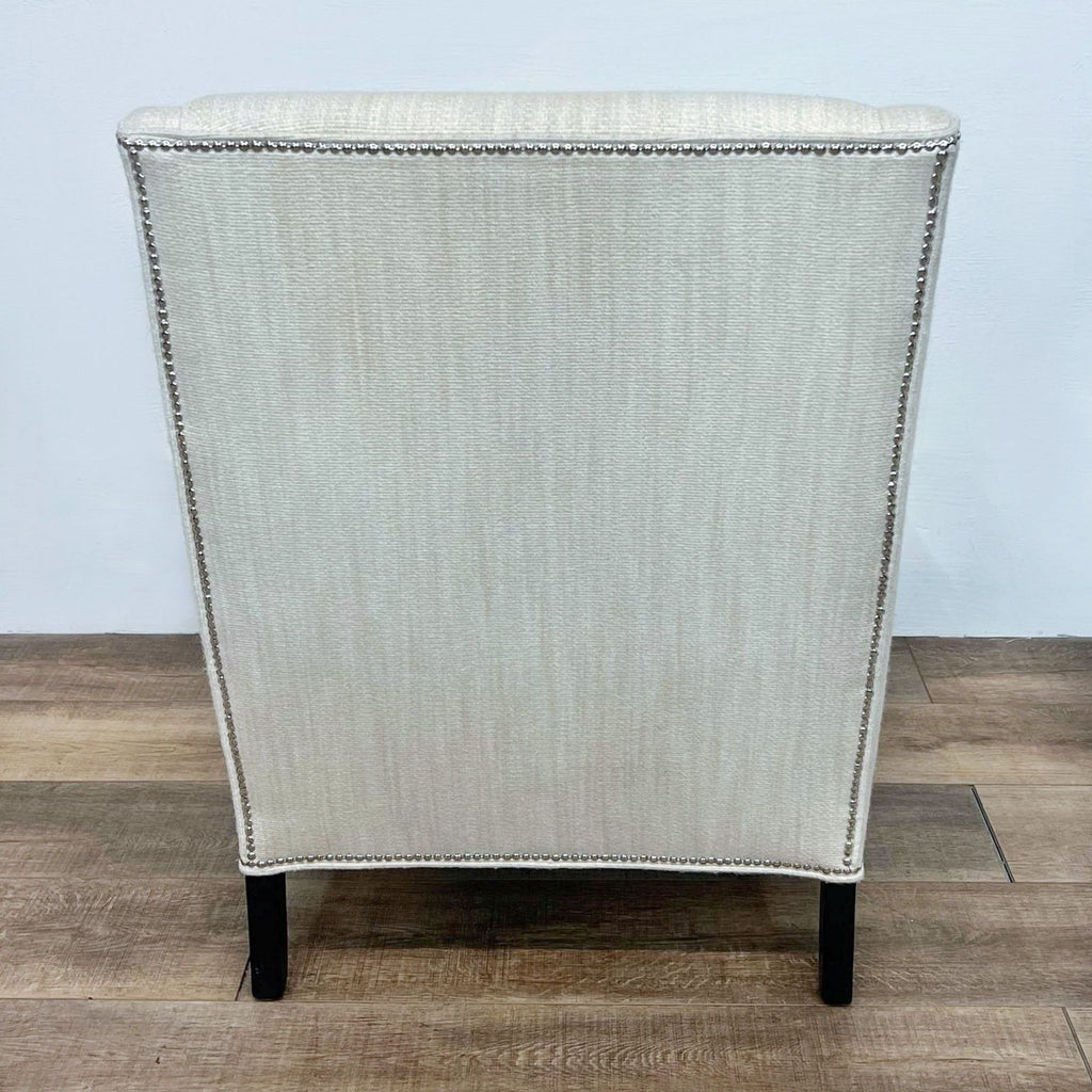 Back view of a cream wingback chair with nailhead trim, highlighting clean lines and dark legs.