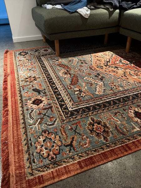 1. Reperch rug with intricate floral and geometric designs, rust border, and blue and beige tones in a living space.