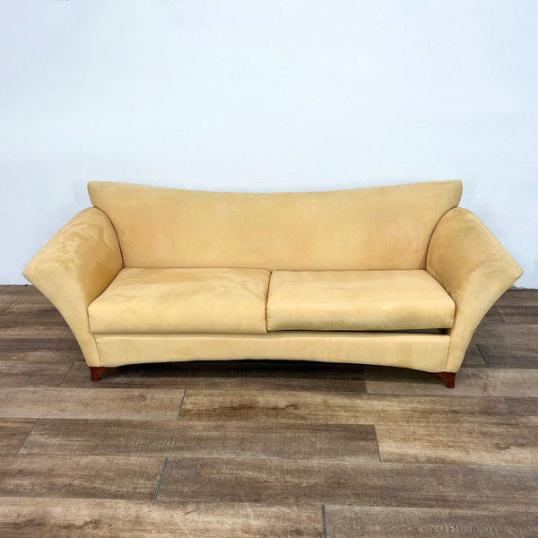 Yellow sofa with flared arms and wooden legs, set on wooden floor.