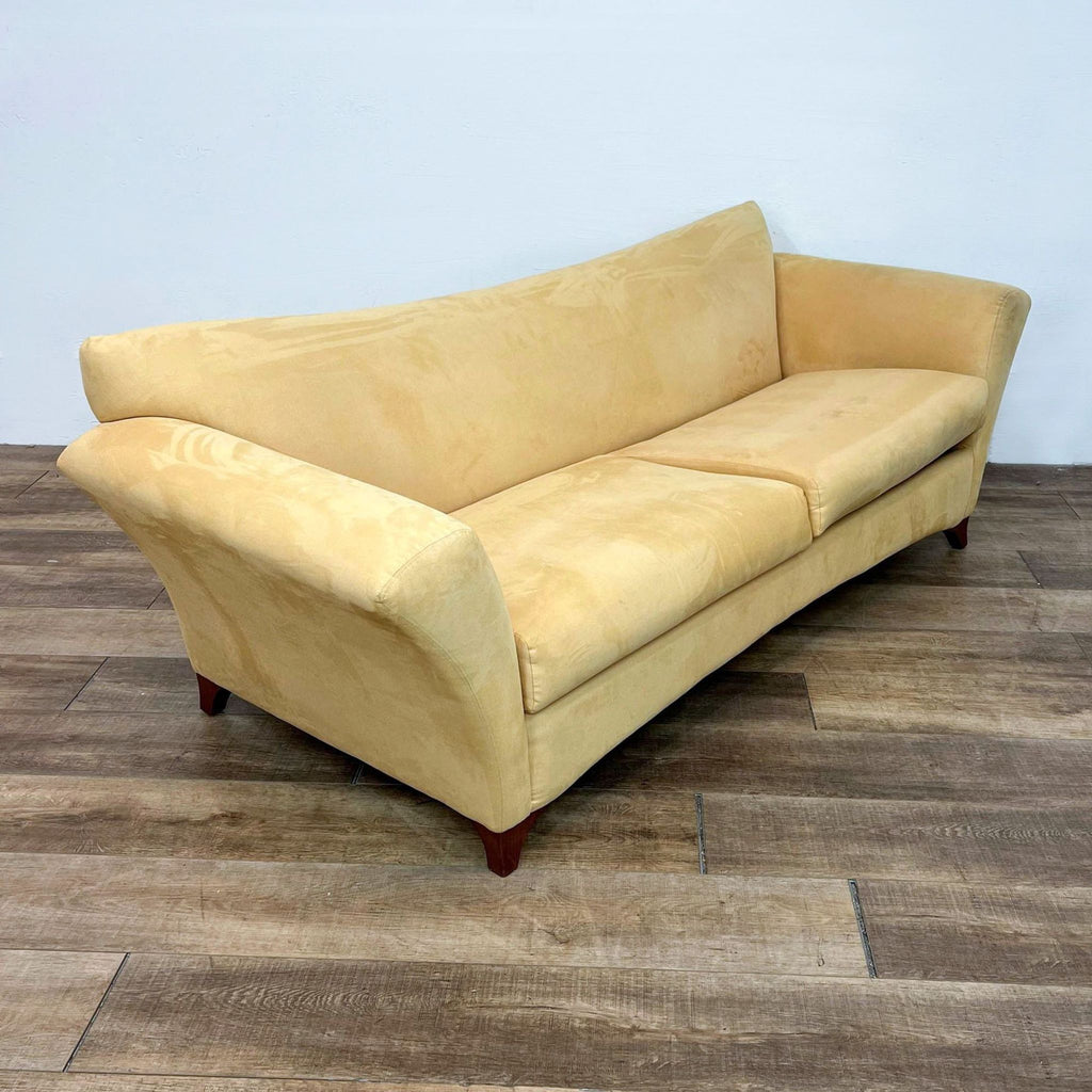 Side view of yellow sofa, featuring flared arms and straight back, on wooden floor.