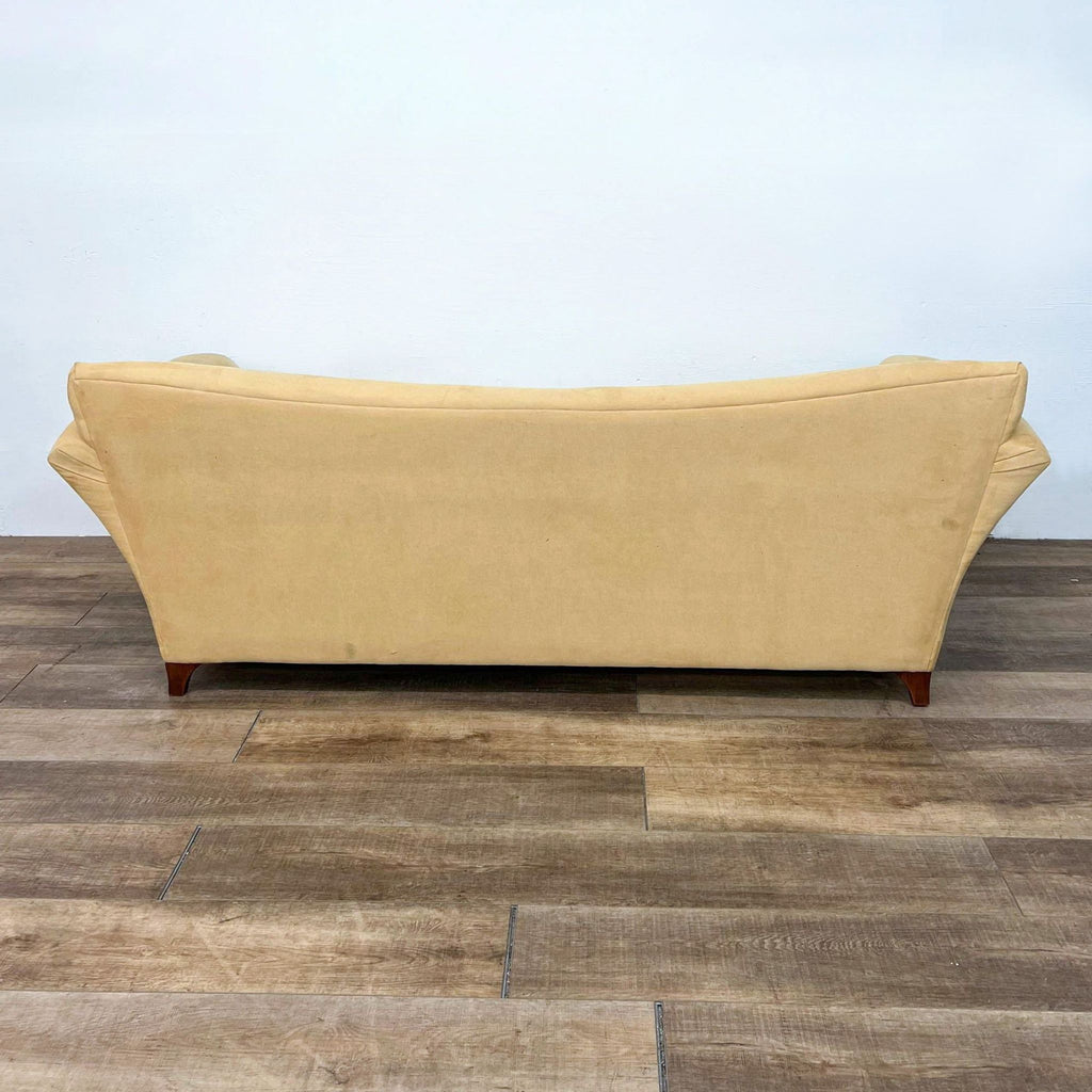 Rear view of flared-arm yellow sofa with wood feet on wooden floor.