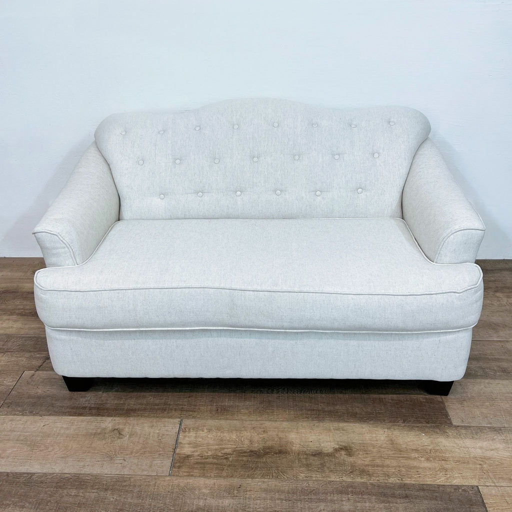 Front view of a button-tufted loveseat with curved back and dark legs.